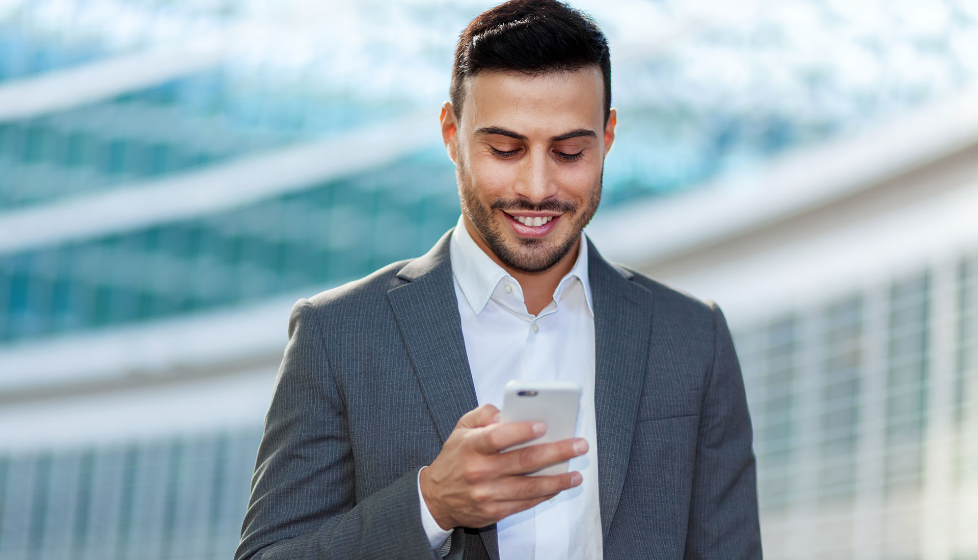 Uomo in abito che sorride mentre usa lo smartphone.