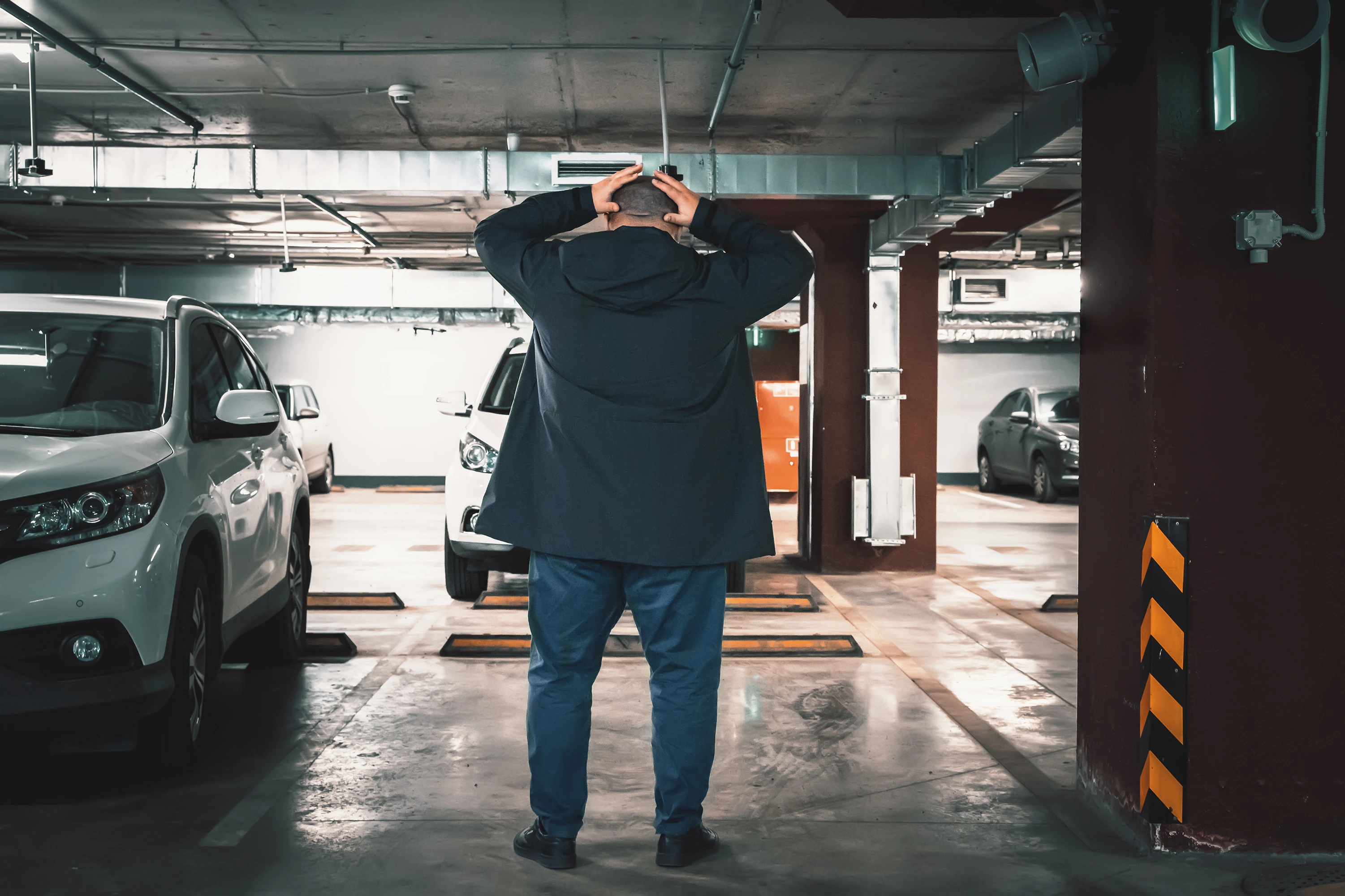 Uomo preoccupato in un parcheggio coperto tra auto parcheggiate.